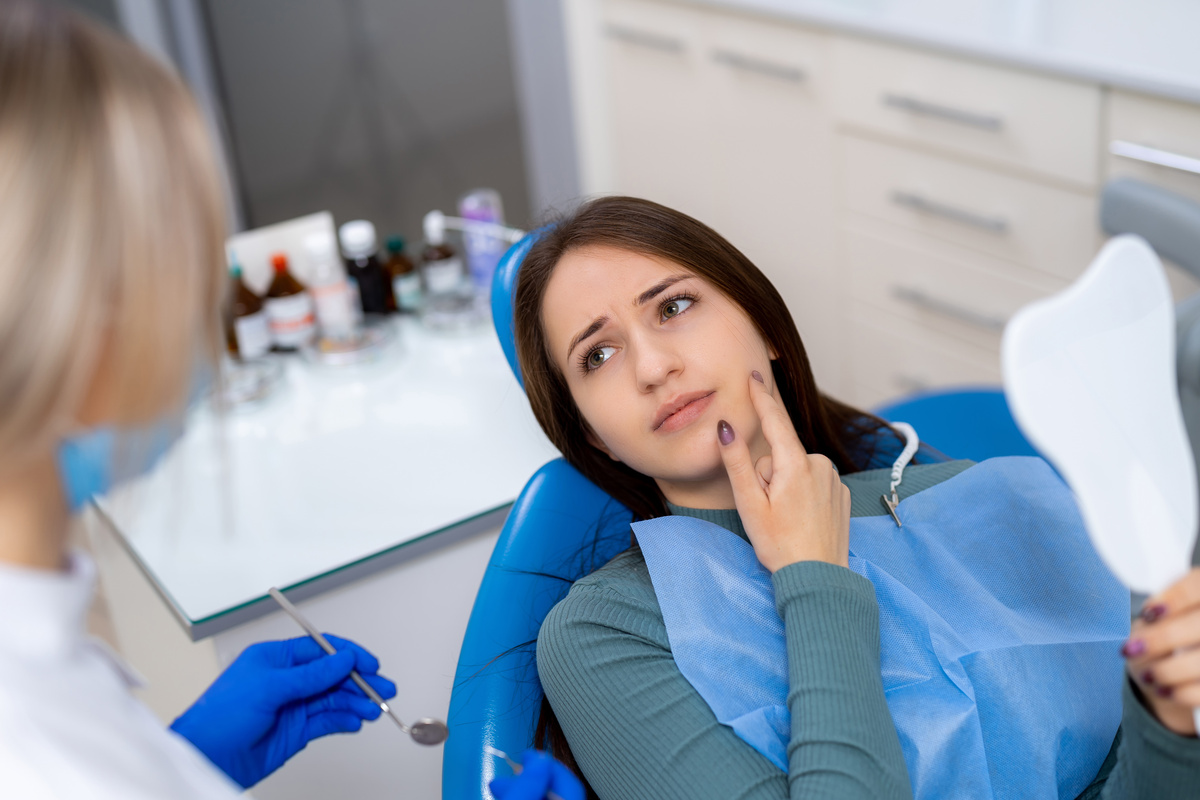 Patient has dental discomfort. A young woman at the dentist shows signs of discomfort while discussing her dental issues with the hygienist.
