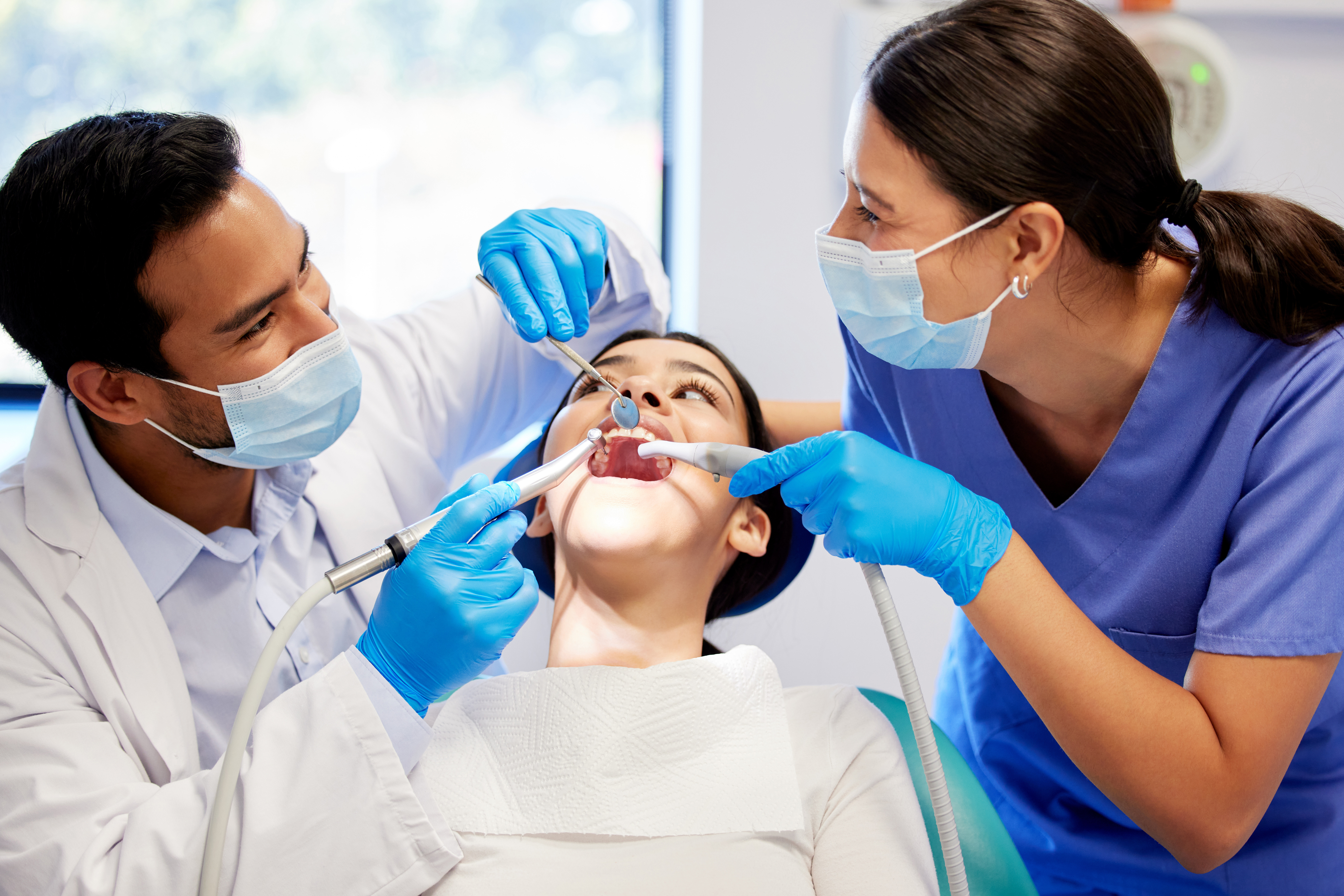 Dentist, team and patient in clinic with equipment for consultation, oral hygiene or medical procedure. Service, doctor man and nurse woman with client for teeth extraction, cleaning or dental care