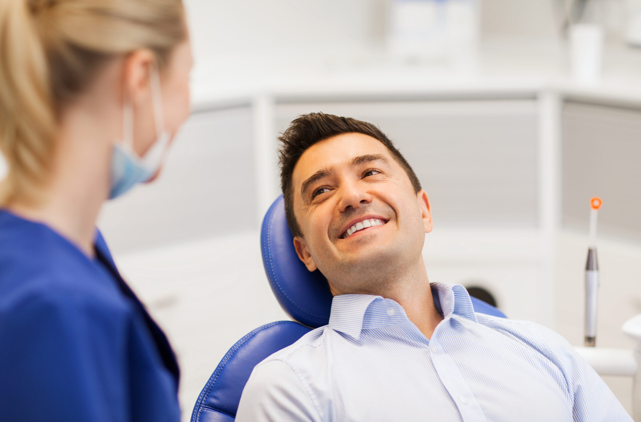 people, medicine, stomatology and health care concept - female dentist talking to happy male patient at dental clinic office
