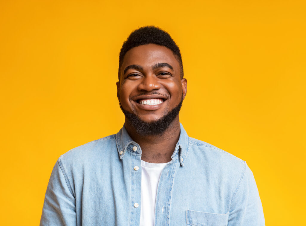 Portrait of young smiling african american guy with beard over yellow background, copy space