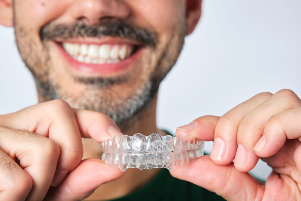 closeup man hand holding transparent retainer with unrecognizable bearded man face in unfocused background on white background