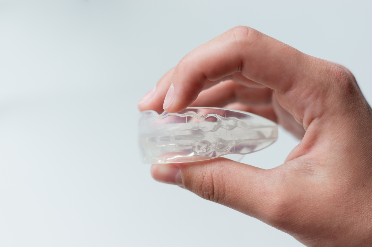 Man holding orthodontic silicone mouth guard for teeth straightening or whitening. Side view, close-up, on white background