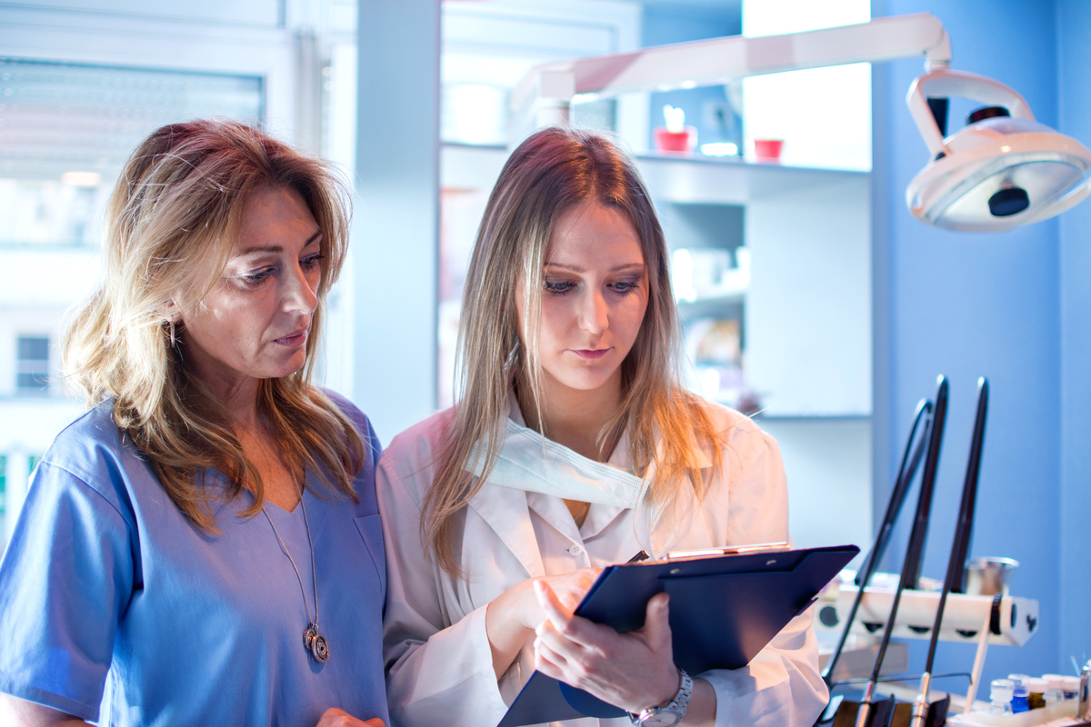 Female nurse and dentist reading patient's dental results from clipboard in dentist's office.