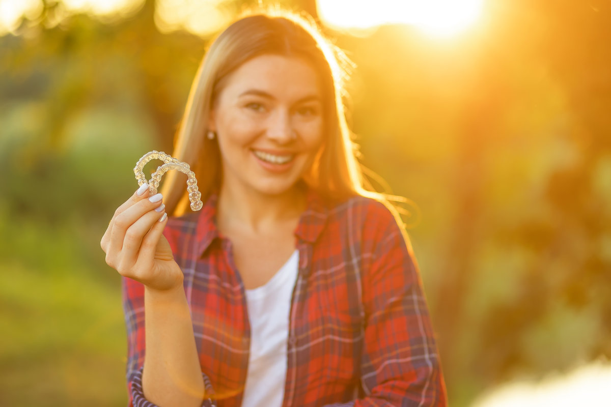 A young smiling woman holding invisalign braces, dental healthcare and Orthodontic concept