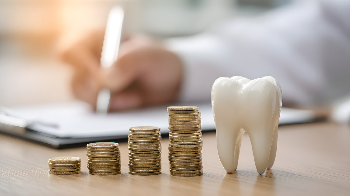 Person signing papers behind a row of increasing coin stacks and a tooth model, symbolizing dental health costs, insurance plans, and finance management