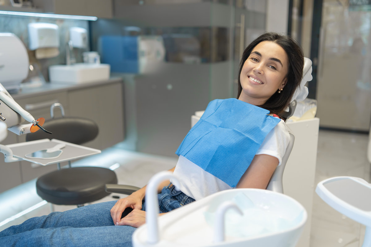 Pretty brunette happy female patient sitting in the chair at dental clinic