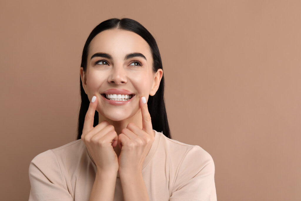 Beautiful woman showing her clean teeth and smiling on beige background, space for text