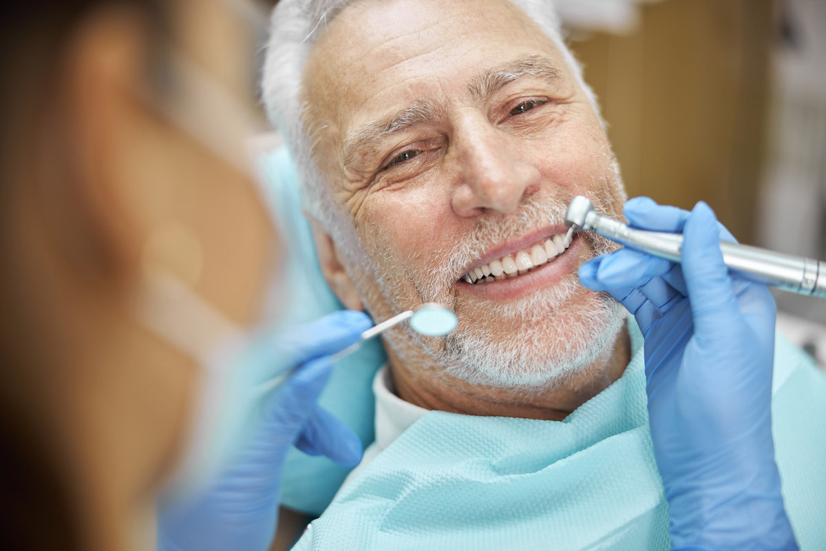 Close-up photo of a cheerful aged man smiling while having his teeth checked for caries and cavities