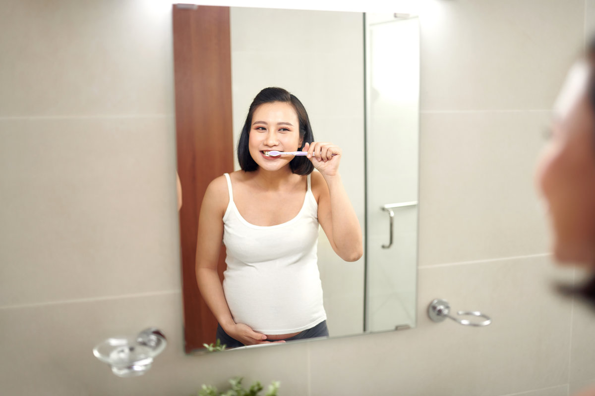 Young pregnant woman brushing teeth in bathroom