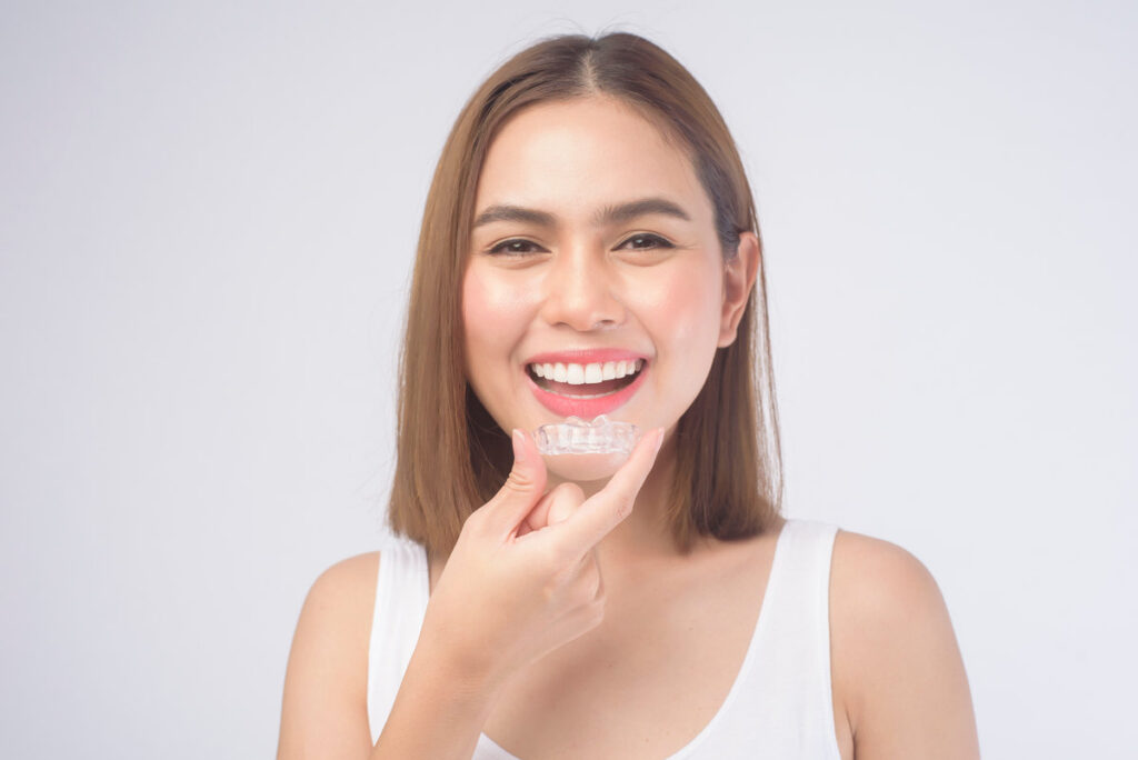 A young smiling woman holding invisalign braces over white background studio, dental healthcare and Orthodontic concept.