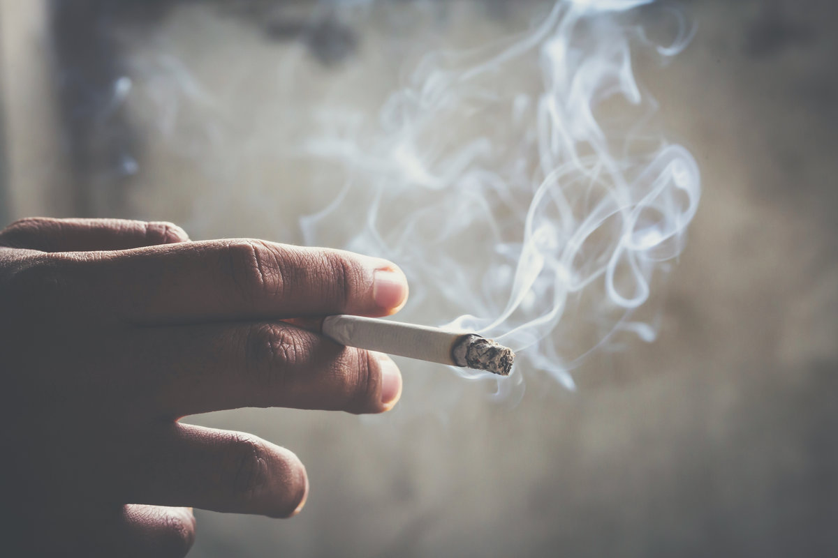 man holding smoking a cigarette in hand. Cigarette smoke spread.