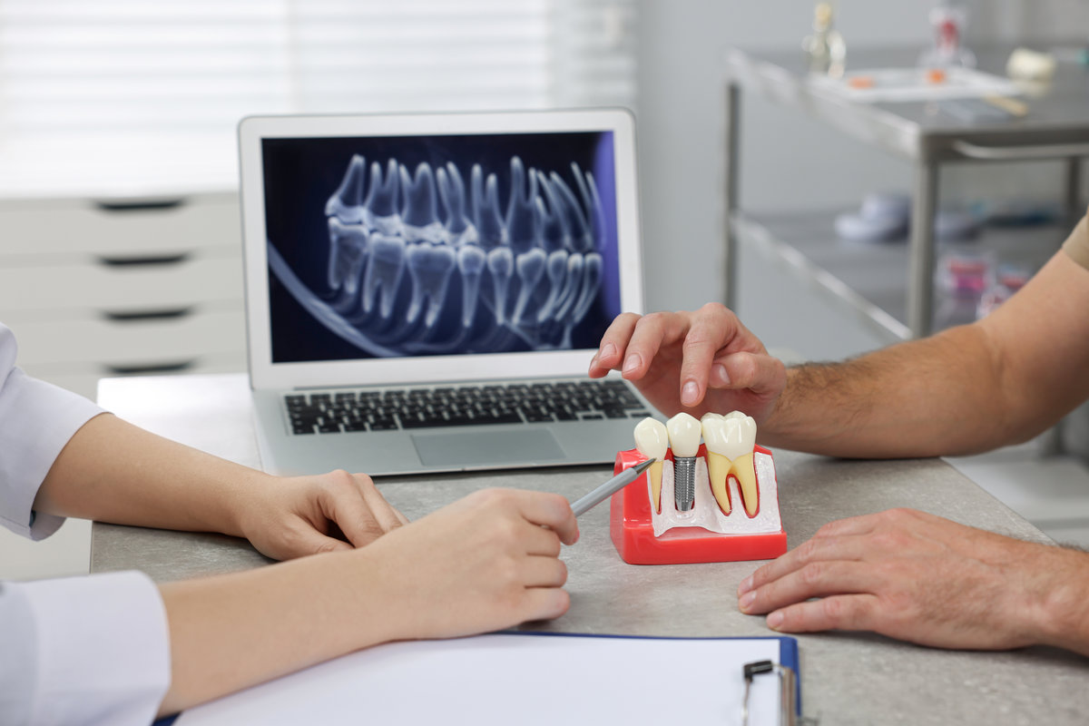 Doctor showing patient educational model of dental implant in clinic, closeup