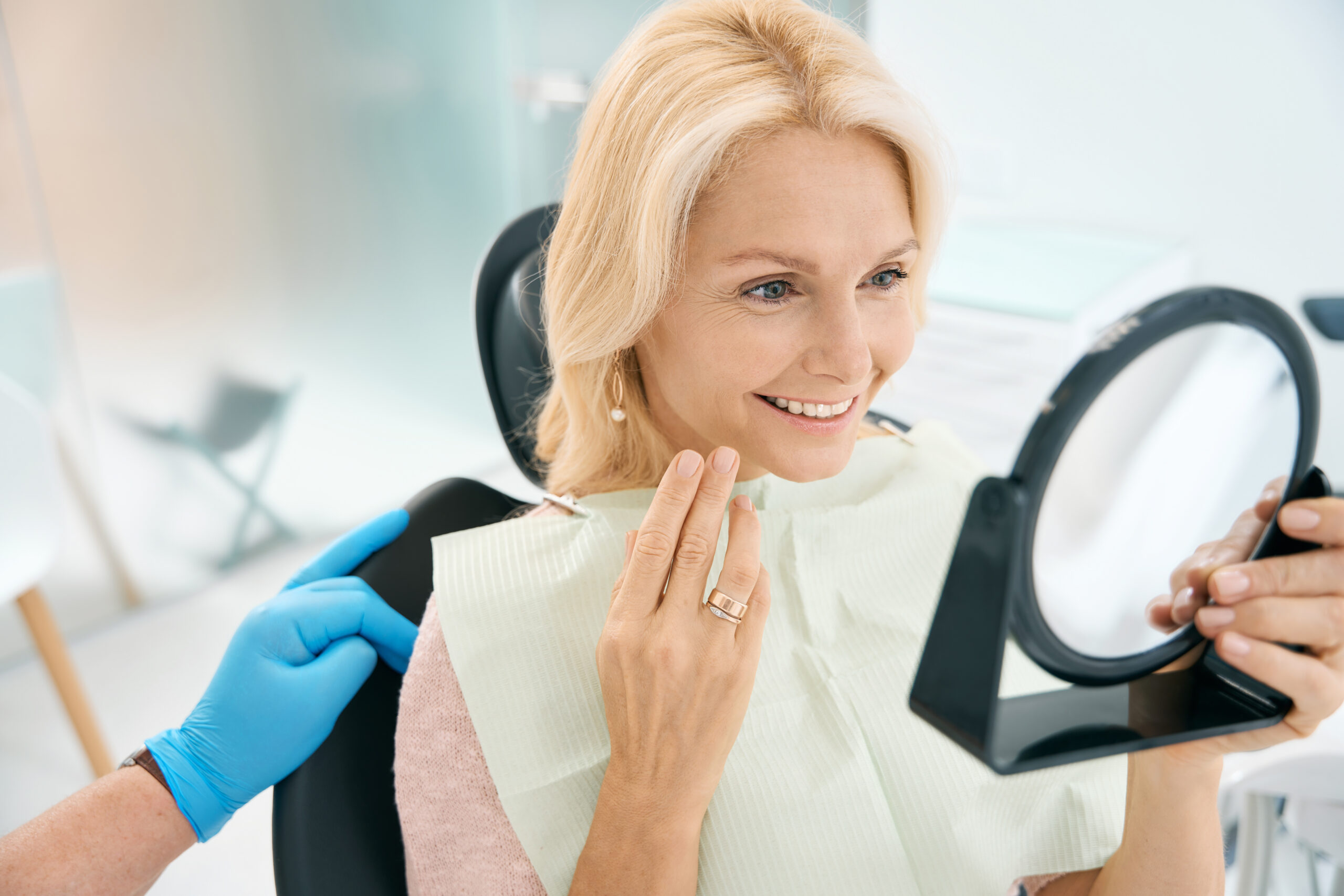 Happy adult woman smiling and looking in dental chair mirror