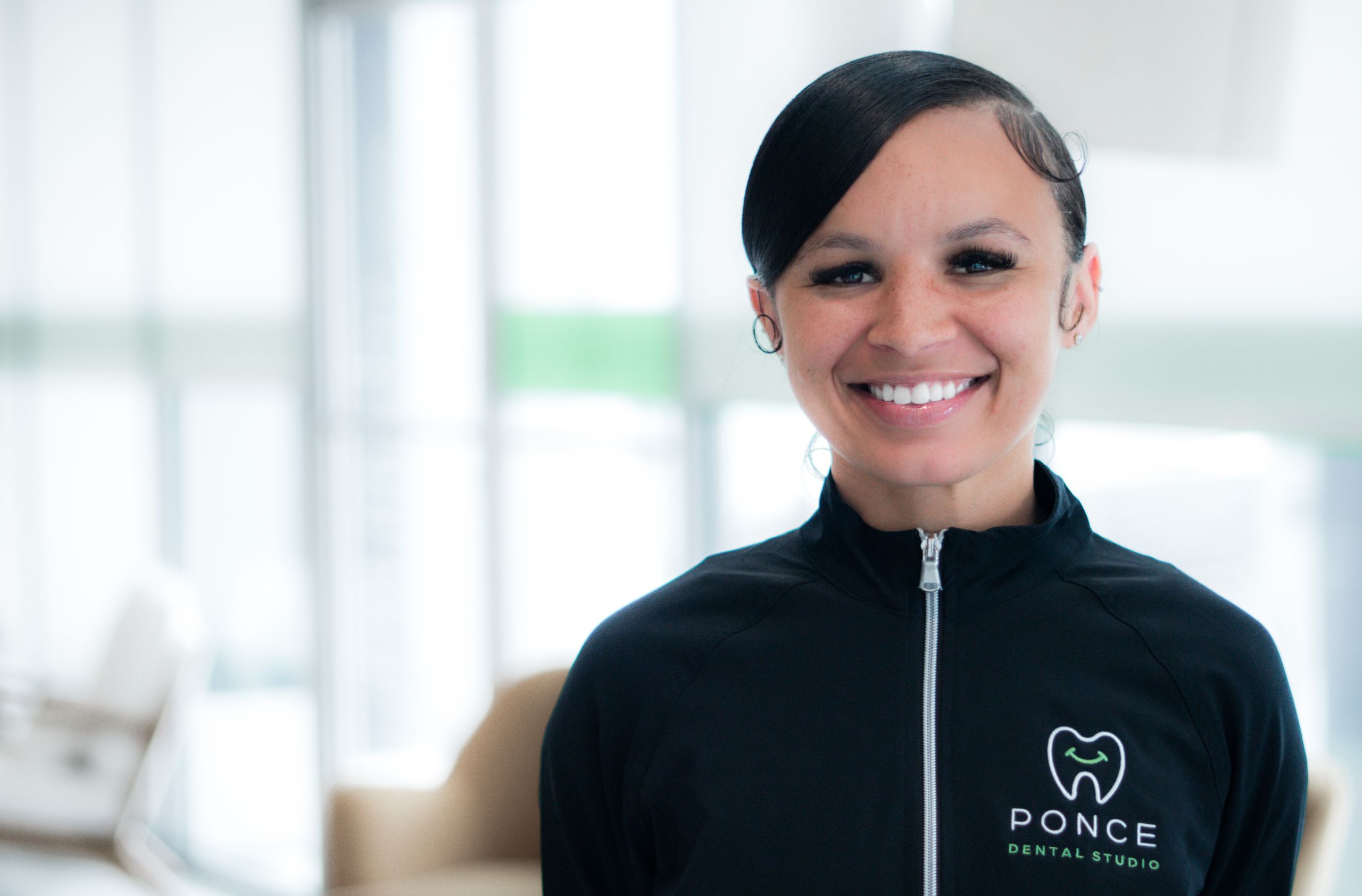 Shae, Ponce Dental Studio staff member in branded black jacket, bright office setting